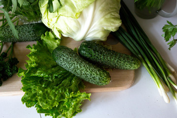 A bunch of fresh lettuce, cabbage, green onions, sliced cucumbers, arugula, parsley on the cutting wooden board on the white background. Seasoning vegetables on a table. Healthy ingredient for salad.