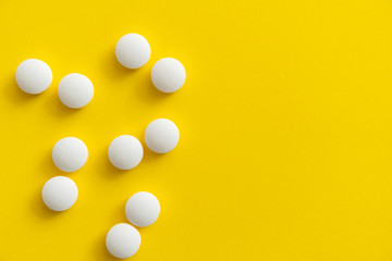White pills on yellow background. Medicine, medication, painkillers, tablet, medicaments, drugs, antibiotic, vitamin, treatment. Pharmacy theme. Top view on the pills scattered on the white surface.