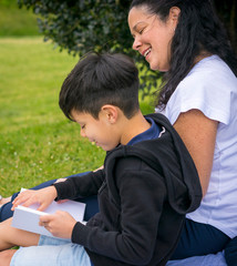 Beautiful portrait of a mother and her son enjoying and reading a good book at the park