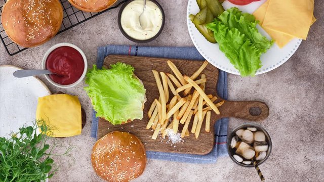 Stop-motion animation. Cook burgers. Cook burger from buns, cutlets, lettuce, cucumber, tomatoes, onions and sauces. Beautiful background.