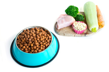 Foreground bowl with dry food for animals and various ingredients of healthy food in the background. Dog food concept