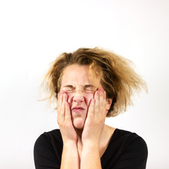 A close-up of a sad girl with disheveled hair, who was suffering and pressed her hands to her face. On white background. An emotion of frustration. Bad hair day.