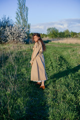 A girl with long hair and a beige trench coat walks along a country road, woman walking in the countryside