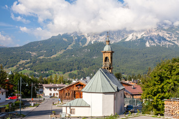 Fototapeta na wymiar An old chapel in an alpine town amid a mountain peak in dense clouds, Cortina D'Ampezzo, Italy