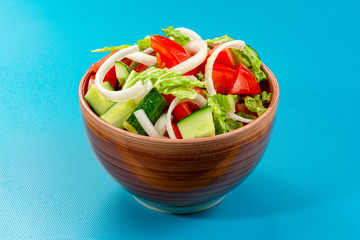 Healthy salad with tomatoes, cucumber, olives, onion, salad in a ceramic bowl on a blue background. Healthy eating concept