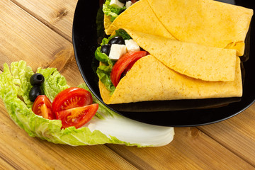 Vegetarian healthy corn tortillas, salad, tomatoes, olives on a wooden table. Selective focus
