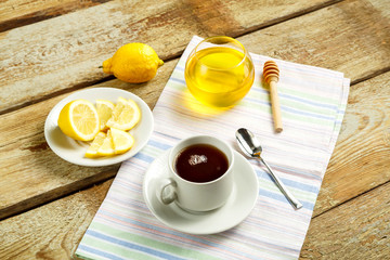 White cup with tea with lemon and honey on a table on a napkin.