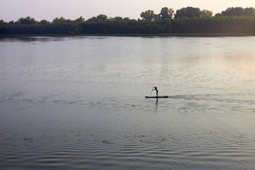 Silhouette of girl standing with a paddle on the SUP surfboard at sunset. Stand up paddle boarding...