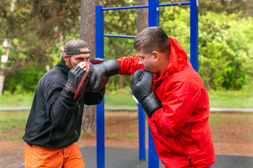 Middle-aged boxer training with coach outdoors