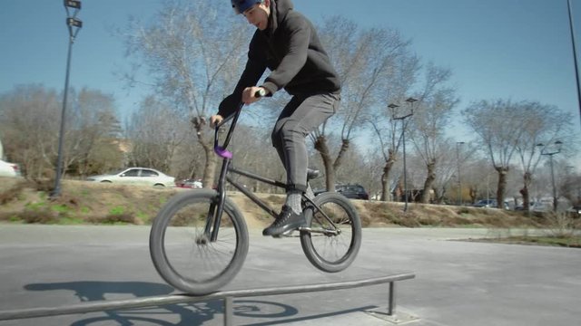 A young bmx rider does tricks on pipe at skate park.
