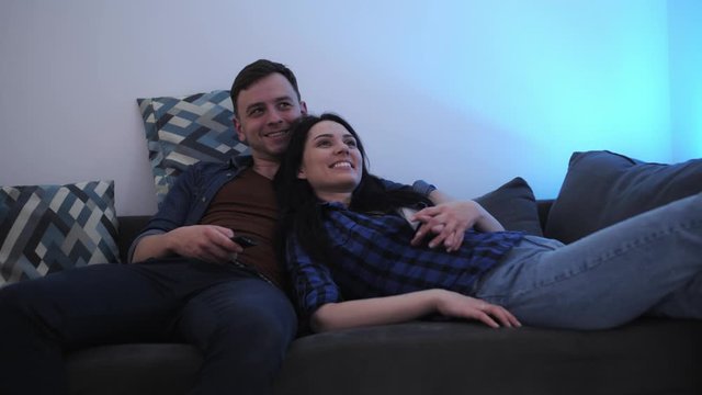 Happy young couple Lying, Hugging and Smiling on couch in new apartment and watching tv.
