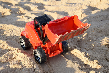 Toy loader on the beach. Orange toy excavator raking sand. The concept of summer holidays, vacations, as well as construction,earthworks