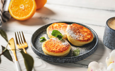 Cottage cheese pancakes on a plate, white wooden table, close-up. Delicious and beautiful breakfast with coffee.