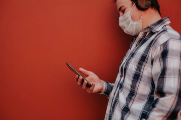 a masked man stands against a red wall and uses a phone.