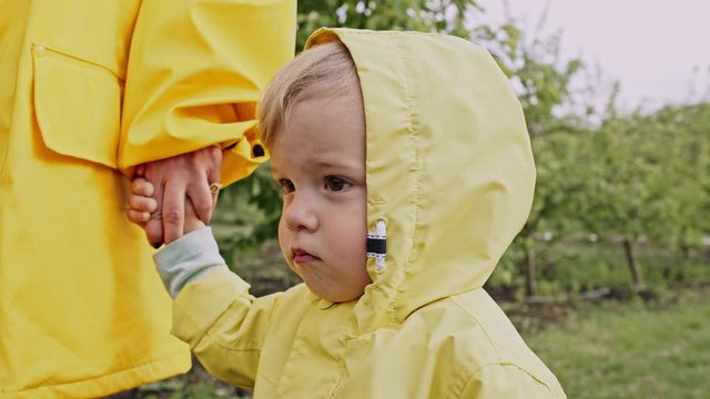  Portrait Of Cute Baby Boy In Yellow Raincoat. Child Holds Mom's Hand. Love, Care, Attachment, Family, Children Concept.