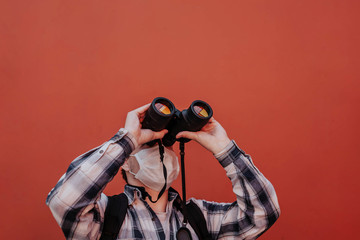 a man looks up through binoculars on a red background