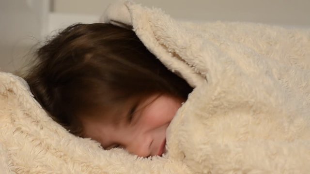 Little charming girl baby lying on the bed under the covers and smiling happy