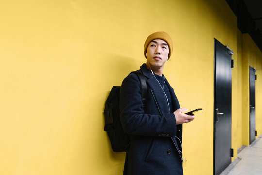 Stylish man with yellow hat and earphones using smartphone