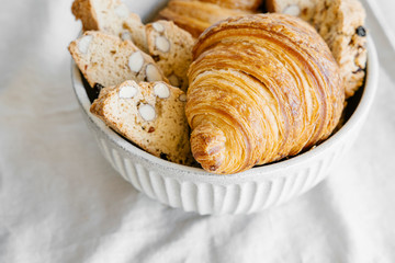 Freshly baked classic croissants and almond biscottis on linen light background. Breakfast food concept. 