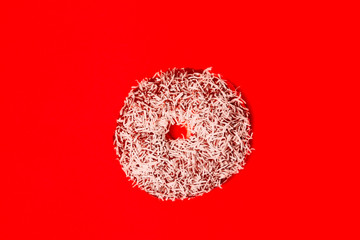 Flat top view of a coconut topping chocolate donut with red background
