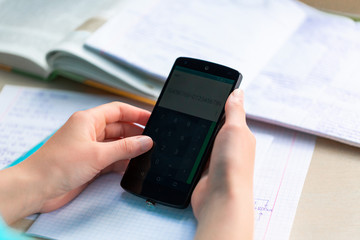 Beautiful young teenage school girl studying with smartphone, close up on hands with the mobile phone.