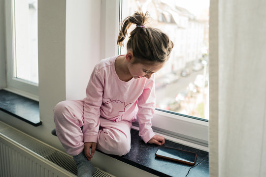 Little girl with smartphone sitting at the window