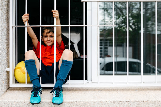 Boy with soccer ball at the window without being able to leave the house to play