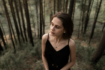 Naklejka na ściany i meble portrait of a girl looking away, standing in a pine forest