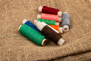 Several coils of multicolored sewing thread against a background of coarse-textured burlap. Close...
