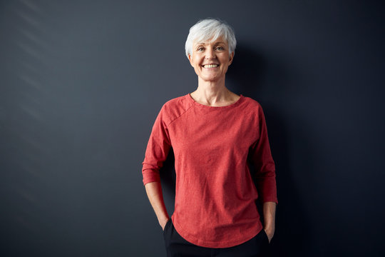 Portrait of smiling senior woman wearing red shirt standing in front of grey wall
