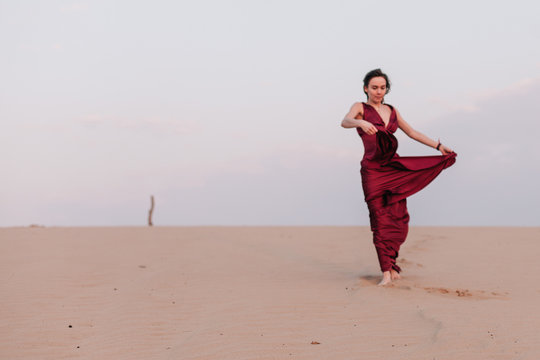 Girl in red dress with cloth in the wind in the desert