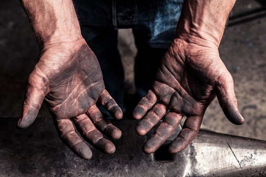 Soot-blackened hands of knife maker over anvil