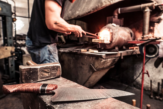 Knife maker working at melting furnace, finished knife on anvil in the foreground