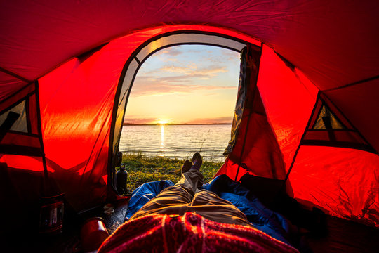Man camping in Estonia, watching sunset lying in tent