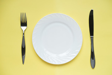 white plate and metal fork and knife on yellow background. reastaurant menu mockup. template for food design. copy space for text and advertising.