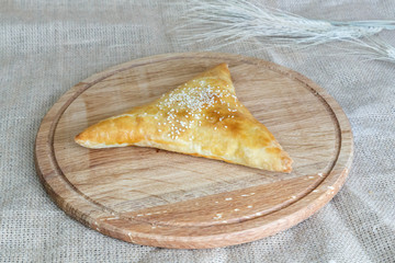  Uzbek triangular samsa of puff pastry on a round kitchen board on a background of burlap