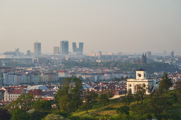 Panoramatic picture of Prague, taken in sunny spring morning after sunset from castle and shown Petrin hill with mix of traditional architecture along the Vltava river and modern buildings at horizon.