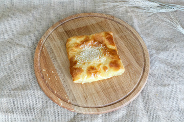 Appetizing Uzbek square samsa made of puff pastry on a round kitchen board on a burlap background