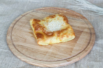 Appetizing Uzbek square samsa made of puff pastry on a round kitchen board on a burlap background