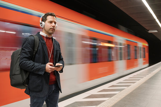 Businessman listening music through mobile phone while standing on platform against subway train