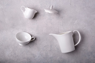 White kettle with lid, milk kettle and white tea cup on a gray concrete background. View from the top.