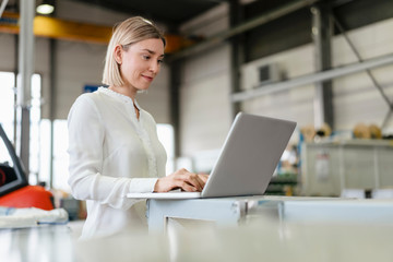 Smiling young woman using laptop in a factory