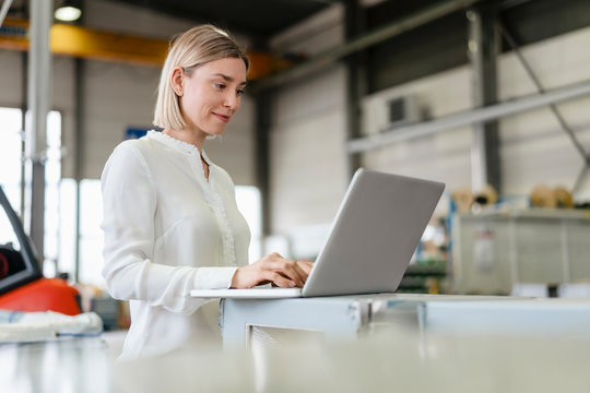 Smiling young woman using laptop in a factory