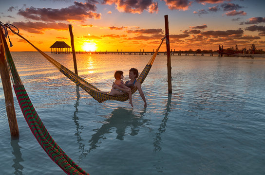 Mother and daughter relaxing on hammock at beach during sunset in Holbox Island, Cancun, Mexico
