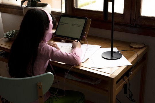 Girl with headphones drawing manga comics while using tablet computer at desk in house