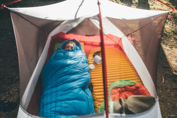 Young woman sleeping in sleeping bag in a tent