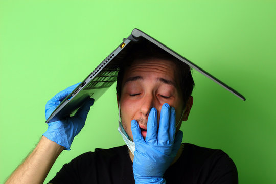 A young man holds a laptop on his head metaphorically depicting the roof of a house. Emotion of fatigue. Work from home concept