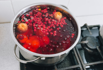 Fresh fruits are boiled in boiling water in a metal pan on the stove. Delicious stewed apricot, apples, cherries, raspberries. Photography, concept.