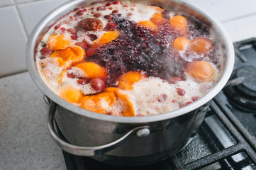 Cooking a delicious compote of apricot, apples, cherries, raspberries. Fresh fruits are boiled in boiling water in a metal pan on the stove. Photography, concept.