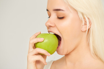 Woman with Apple. Beautiful girl closeup eating an apple on a gray background, healthy teeth. High Resolution Image